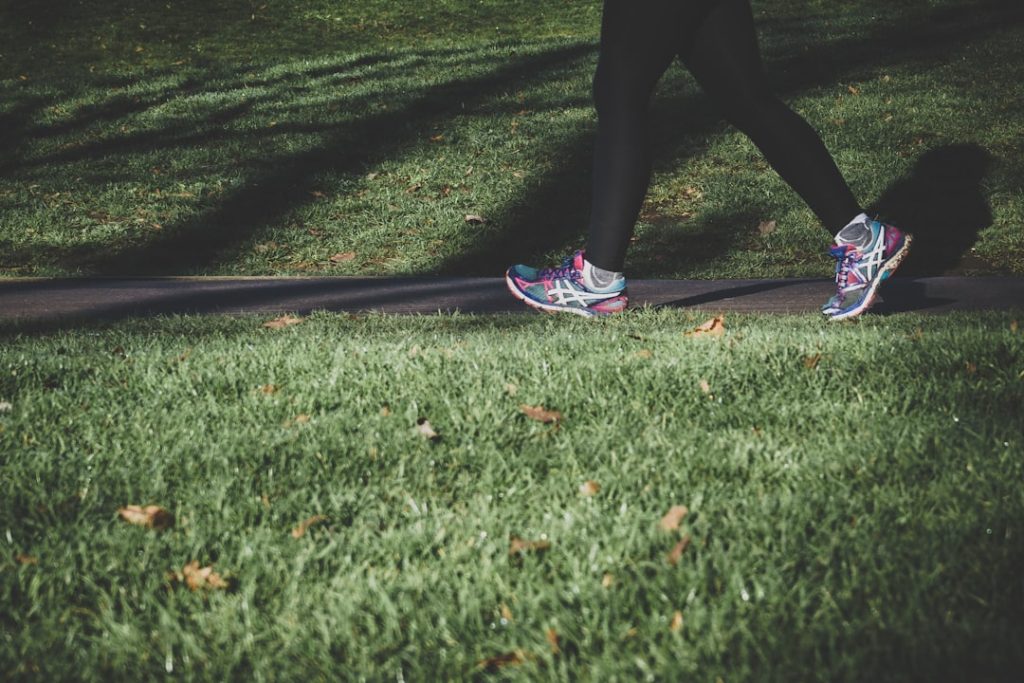 A person walking on a path beside grass, wearing colorful Asics running shoes. Photo by Arek Adeoye on Unsplash.